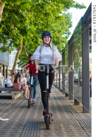 Trendy fashinable teenager girls riding public rental electric scooters in urban city environment. New eco-friendly modern public city transport in Ljubljana, Slovenia 67937641
