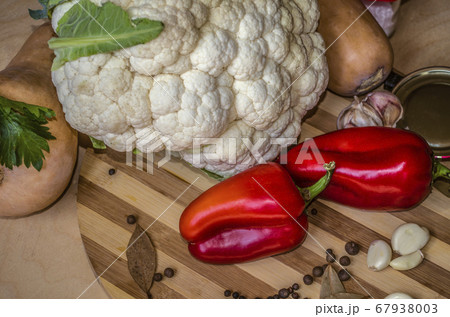 Round wooden chopping board with red pepper, garlic, cauliflower, pumpkin with spices and celery leaves 67938003