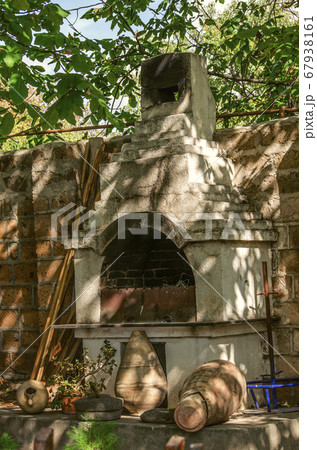 An old barbecue oven, with ancient clay pots and stone millstones under trees in a rural courtyard 67938161
