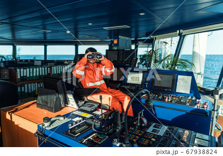 Filipino deck Officer on bridge of vessel or ship looking through binoculars Filipino deck Officer on bridge of vessel or ship looking through binoculars 67938824