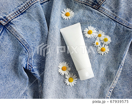 Mock-up of unbranded white bottle tube and chamomile flowers on a blue jeans background. Top view. Natural organic spa cosmetics concept. 67939575