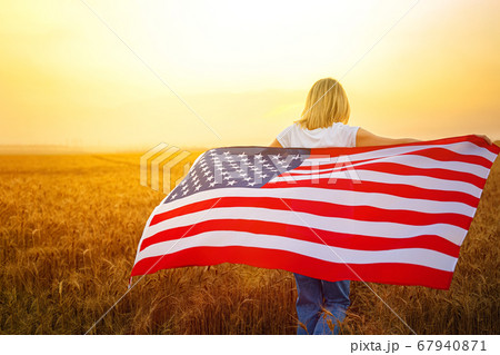 Woman running and jumping carefree with open arms over wheat field Holding USA flag 67940871