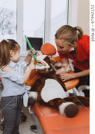Little girl and dentist checking teeth of toy Little girl and dentist checking teeth of toy 67942152