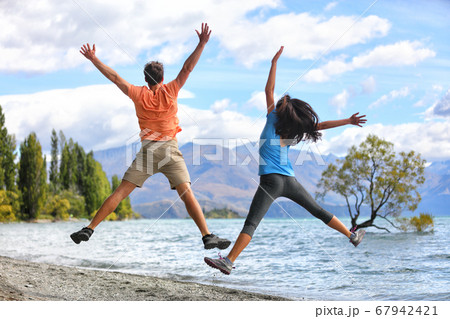 New Zealand tourists couple jumping of happiness at Wanaka Lone . Happy young people doing funny jump of joy sightseeing traveling in summer adventure destination. Woman and man 67942421