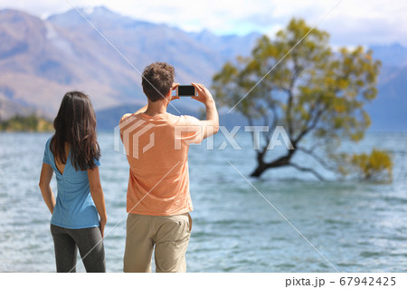 New Zealand tourists taking phone pictures of Wanaka Lone Tree at lake. People looking at view of famous touristic attraction in south island, Otago Region, NZ 67942425