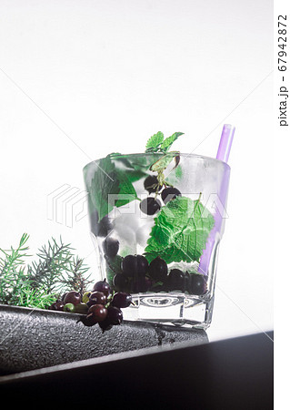 berry cocktail, mint, ice in a rox glass on the edge of a bar counter white background. bot view, close up, vertical orientation 67942872