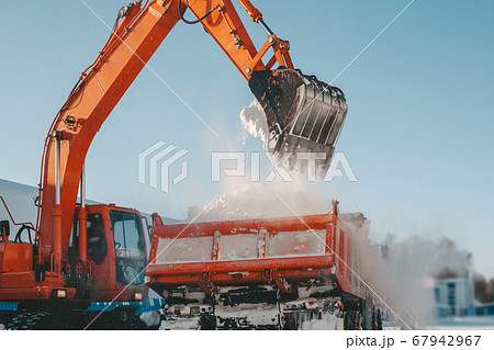 Snow removal after snowfall and blizzards. Excavator loads snow into a truck Snow removal after snowfall and blizzards. Excavator loads snow into a truck 67942967