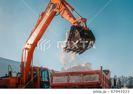 Snow removal after snowfall and blizzards. Excavator loads snow into a truck 67943025