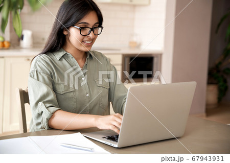 Smiling indian young woman typing on laptop computer working at home office. 67943931