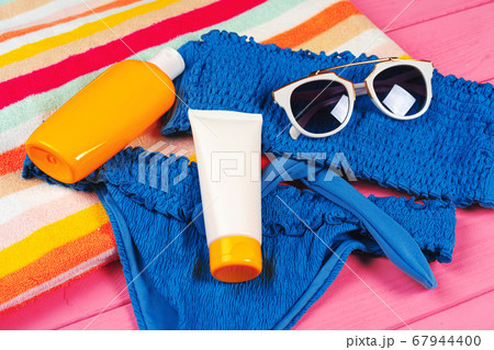 Blue bikini with sunblock cream bottle on bright pink wooden background 67944400