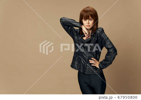 Young beautiful woman posing on a beige background in the studio in a black leather jacket Young beautiful woman posing on a beige background in the studio in a black leather jacket 67950800