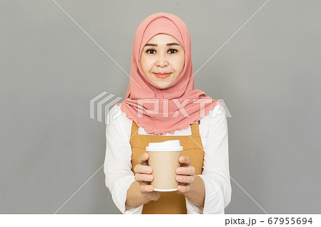 Small business owner happy young beautiful asian muslim woman propose hand arm paper cups hot beverage invite visit cafe wear traditional dress and brown apron isolated gray background Small business owner happy young beautiful asian muslim woman propose hand arm paper cups hot beverage invite visit cafe wear traditional dress and brown apron isolated gray background 67955694