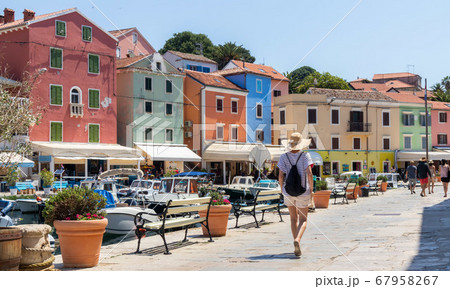 Rear view of beautiful blonde young female traveler wearing straw sun hat sightseeing and enjoying summer vacation in an old traditional costal town of Veli Losinj, Adriatic cost, Croatia Rear view of beautiful blonde young female traveler wearing straw sun hat sightseeing and enjoying summer vacation in an old traditional costal town of Veli Losinj, Adriatic cost, Croatia 67958267