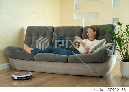 Attractive girl using smartphone while robotic vacuum cleaner cleaning house Attractive girl using smartphone while robotic vacuum cleaner cleaning house 67960188