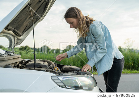 Woman standing near the broken car. The girl opened the hood and look at the engine.  67960928