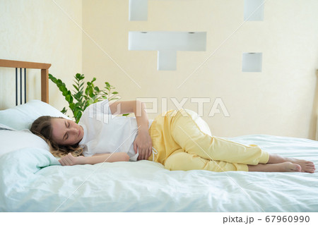 Woman suffering from abdominal pain while lying on bed at home Woman suffering from abdominal pain while lying on bed at home 67960990