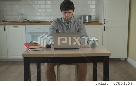 Young man works at home on a laptop in a shirt without pants Young man works at home on a laptop in a shirt without pants 67961353