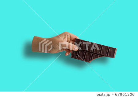 Close-up Of Cropped Hand Holding Broken Milk Chocolate Bar Over Blue Background 67961506