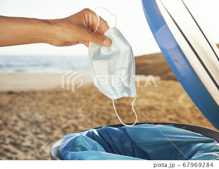 man throws used mask to the trash can on the beach 67969284