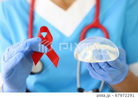 Doctor holds breast implant and red ribbon in his hand. 67972291