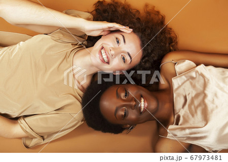 two pretty girls african and caucasian blond posing cheerful together on browm background, etnithity diverse lifestyle people concept two pretty girls african and caucasian blond posing cheerful together on browm background, etnithity diverse lifestyle people concept 67973481