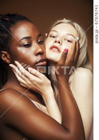 two pretty girls african and caucasian blond posing cheerful together on browm background, etnithity diverse lifestyle people concept 67976741