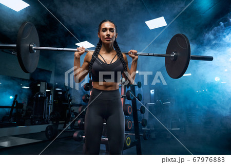 Woman holding barbell on shoulders in gym. Woman holding barbell on shoulders in gym. 67976883