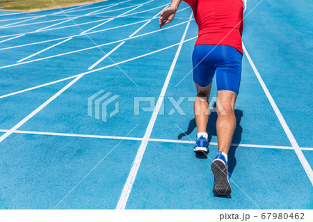 Runner athlete starting running at start of run track on blue running tracks at outdoor athletics and fiel stadium. Sprinter. Sport and fitness man lower body, legs and running shoes sprinting. 67980462