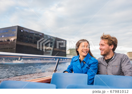 Copenhagen tourists couple on city boat cruise tour enjoying view of the black diamond Royal library, famous architecture building, Denmark, Europe travel. People traveling. 67981012