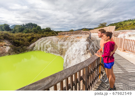 New Zealand travel tourists looking at green pond. Tourist couple enjoying famous attraction on North Island, geothermal pools at Waiotapu, Rotorua. 67982549