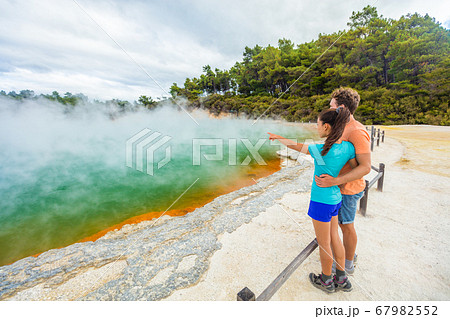New Zealand travel tourists couple at Champagne pool at Wai-O-Tapu pools Sacred Waters. Tourist attraction in Waiotapu, Rotorua, north island. Active geothermal area, Okataina Volcanic Centre, Taupo. 67982552