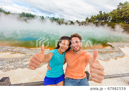 New Zealand happy tourist couple doing thumbs up at famous attraction travel destination. Champagne pool, Waiotapu. Active geothermal area, in Taupo Volcanic Zone, Rotorua, north island. 67982559