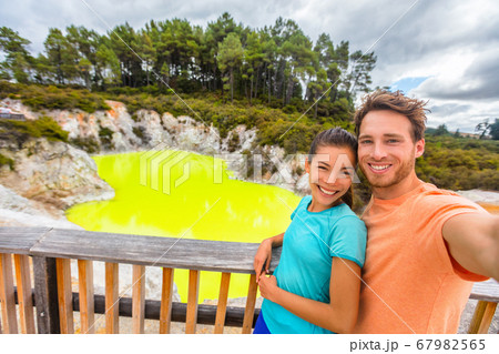 New Zealand tourist attraction couple tourists taking selfie travel destination, Waiotapu. Active geothermal green pond, Rotorua, north island. 67982565