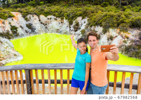 New Zealand tourist attraction couple tourists taking selfie travel destination, Waiotapu. Active geothermal green pond, Rotorua, north island, Wai-O-Tapu, New Zealand. New Zealand tourist attraction couple tourists taking selfie travel destination, Waiotapu. Active geothermal green pond, Rotorua, north island, Wai-O-Tapu, New Zealand. 67982568