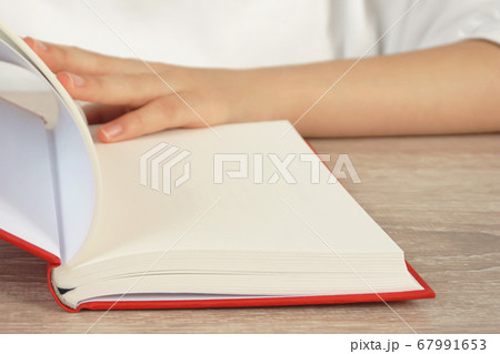 夕暮れ時に本を読む女性。テーブルで本を読む人のクローズアップ 夕暮れ時に本を読む女性。テーブルで本を読む人のクローズアップ 67991653