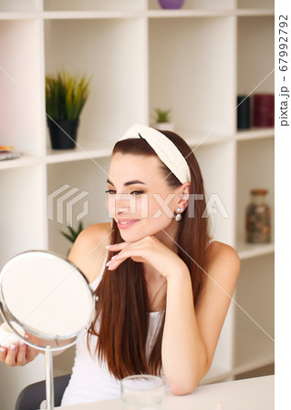 Smiling beautiful girl apply facial skin cream to look in the mirror Smiling beautiful girl apply facial skin cream to look in the mirror 67992792