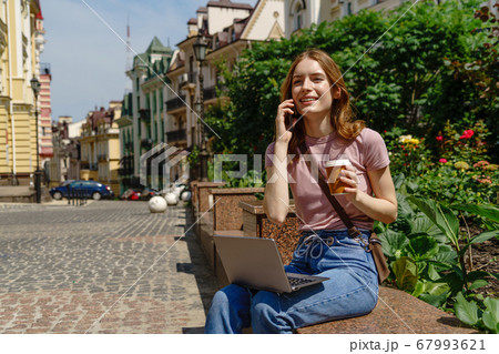 Beautiful Young Woman tourist with takeout coffee in the City Center using laptop Beautiful Young Woman tourist with takeout coffee in the City Center using laptop 67993621