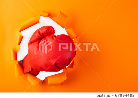 Punching boxing glove though over orange paper 67994488