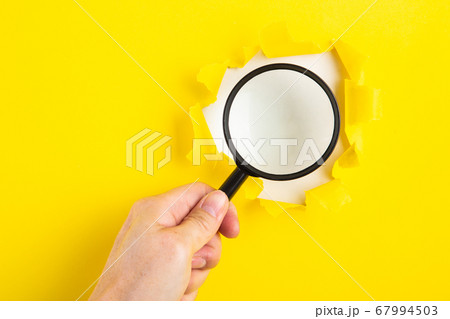 A human hand holds a magnifying glass through a A human hand holds a magnifying glass through a 67994503