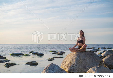 Young woman meditating near sea 67995773