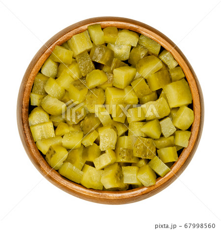 Pickled cucumber, diced, also known as pickle or gherkin, in wooden bowl. Small pickled cucumbers with bumpy skin, cut into cubes. Baby pickles. Close-up from above, over white, isolated food photo. 67998560