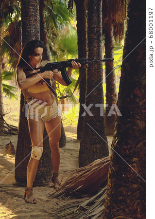 Athletic woman holding gun posing in palm trees Athletic woman holding gun posing in palm trees 68001197