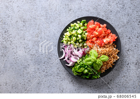 Salad of whole grain cereal spelt with vegetables, tomato, cucumber, greens on grey stone table with space for text. Salad of whole grain cereal spelt with vegetables, tomato, cucumber, greens on grey stone table with space for text. 68006545