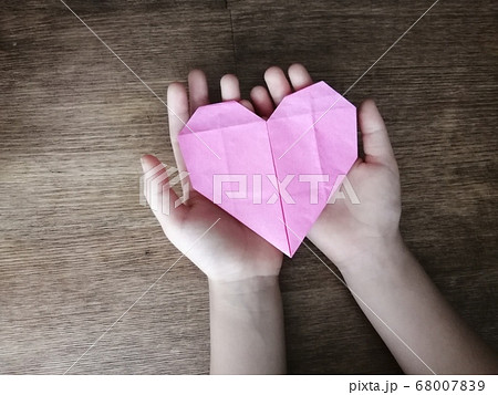 ピンクの折り紙のハートを持つ子どもの写真素材