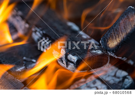 Flame incinerates firewood and transforms it ashes, close up, shallow depth of field. Blaze in a large stove. Nature texture of fire. The flame of fire burns in the brazier, smoldering firewoods. 68010568