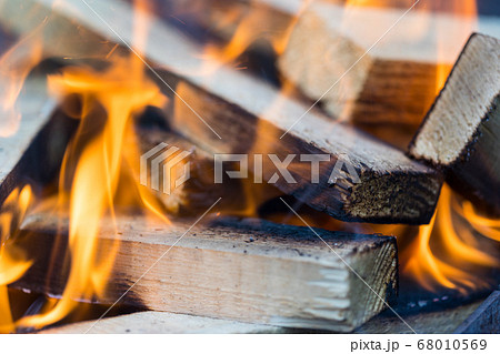 Flame incinerates firewood and transforms it ashes, close up, shallow depth of field. Blaze in a large stove. Nature texture of fire. The flame of fire burns in the brazier, smoldering firewoods. 68010569