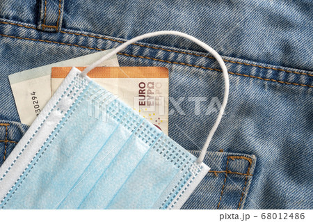Euro banknotes and protective medical mask close-up on blue jeans. The idea of unemployment and the coronavirus pandemic 68012486