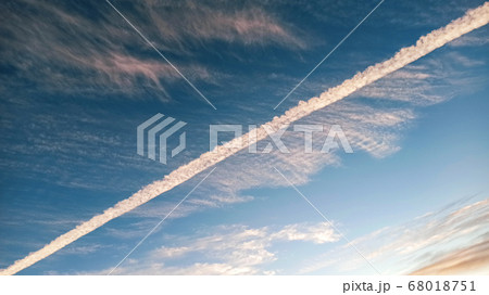 Pattern of airplane trails cutting blue sky in half. Airplane leaving behind a long white trail at the clear blue sky. 68018751
