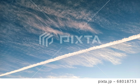 Pattern of airplane trails cutting blue sky in half. Airplane leaving behind a long white trail at the clear blue sky. 68018753
