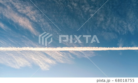 Pattern of airplane trails cutting blue sky in half. Airplane leaving behind a long white trail at the clear blue sky. 68018755